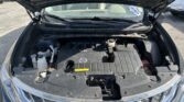 Front view of a car with the hood raised, exposing the engine bay and V6 engine cover beside the Nissan badge in the grille.