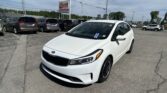 White Kia in the foreground at a used car lot with a row of minivans and an EZ Loan Auto Sales sign in the background.