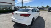 White Kia Forte in a car dealership lot with a Toyota building in the background on a sunny day.