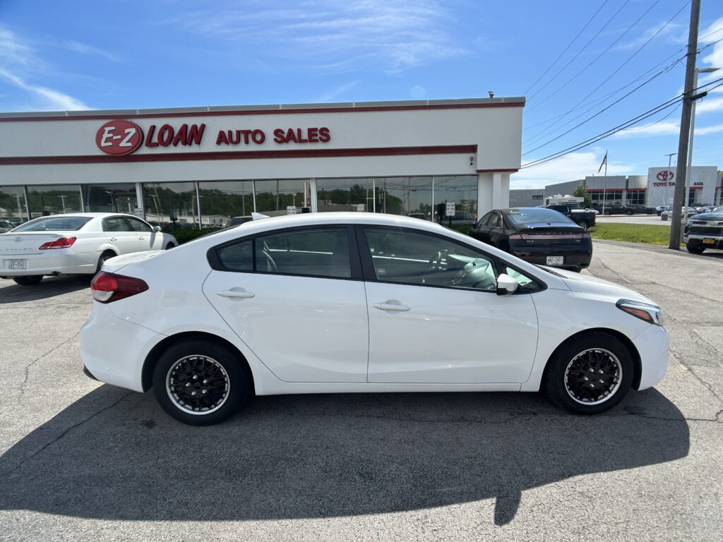 White sedan parked in front of an E-Z Loan Auto Sales storefront on a sunny day with a blue sky above.