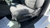 Interior view of a car’s front seats and center console, including the gear shifter and seat belts, with sunlight on gray upholstery.