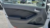 Interior of a car door showing armrest, window controls, and speaker; view through open door to a parking lot with various cars and a Toyota dealership sign in the distance