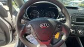 Inside a car cockpit from the driver's seat, steering wheel with Kia logo and dashboard gauges visible outside and center console to the right.