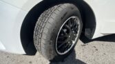 Close-up of a black alloy wheel and tire within the front wheel well of a white car.