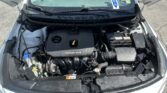 Under-hood view of a white Kia, showing the engine bay with a DOHC 16V engine cover and battery on the passenger side
