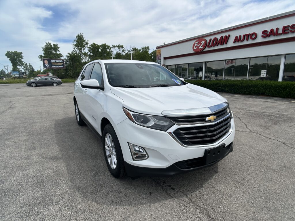 White Chevrolet SUV in a dealership lot with EZ Loan Auto Sales building in the background and trees to the left.