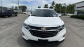 Front view of a white Chevrolet SUV in a car dealership lot, with other vehicles and a building in the background.