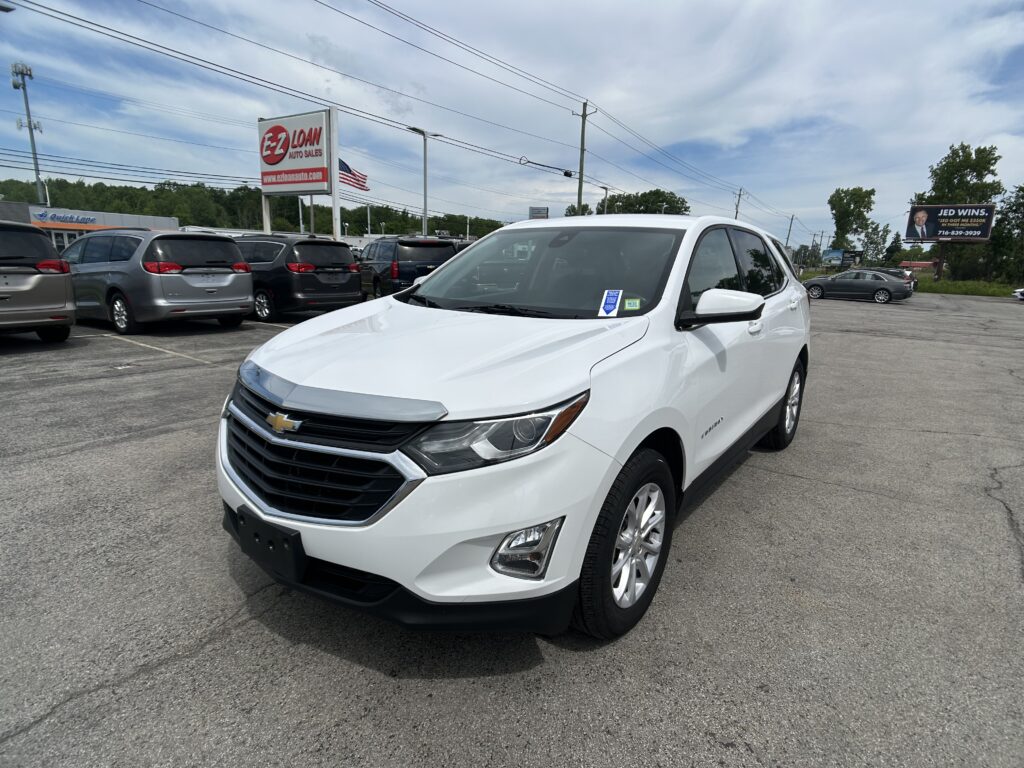 White Chevrolet SUV in the foreground at a car dealership lot with other vehicles and signs in the background.
