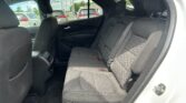 Back seat area of a car with black cloth seats, visible seat belts, and a view of parked vehicles through the rear window.