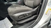 Front interior of a car showing the front passenger seat with hexagonal-stitch fabric, center console, and door frame visible with a seatbelt buckle nearby.