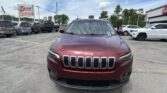 Close-up view of a red Jeep front grille and hood in a car dealer lot, with an E-Z Loan Auto Sales sign visible in the background.