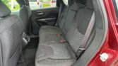 Back seat of a red car with black fabric upholstery, three headrests, and visible seat belts in the rear passenger area.