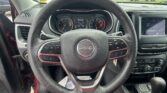 View from driver seat showing a Jeep steering wheel with gauge cluster and center touchscreen, outside car lot visible through windshield