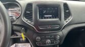 Interior of a car showing the center touchscreen climate controls, gear shifter, and steering wheel, with a parking lot visible through the windshield.