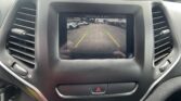 In-dash rearview camera display showing a parking lot with cars on both sides and colored guide lines (green, yellow, red) to assist backing up