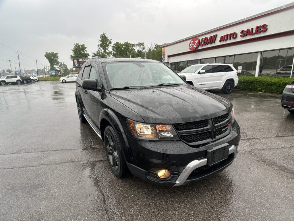 Black Dodge SUV in the foreground on a wet parking lot near an EZ Loan Auto Sales storefront.