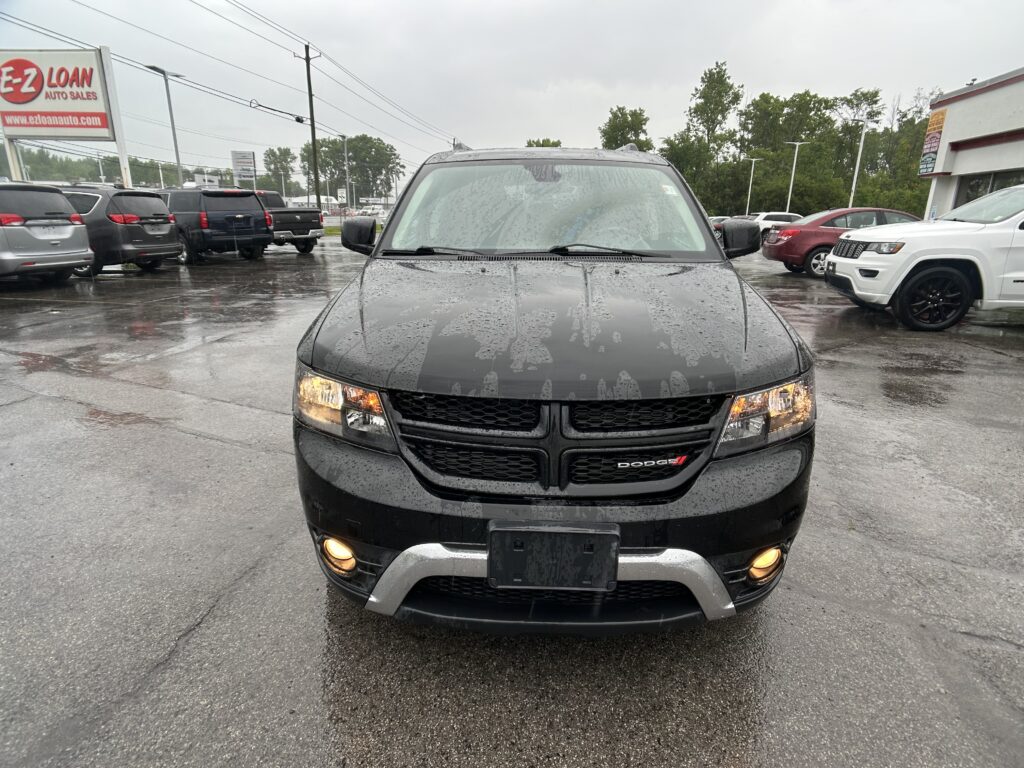 Front view of a black Dodge SUV in a rainy used-car lot with other vehicles parked nearby and headlights on.