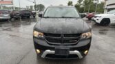Front view of a black Dodge SUV in a rainy used-car lot with other vehicles parked nearby and headlights on.