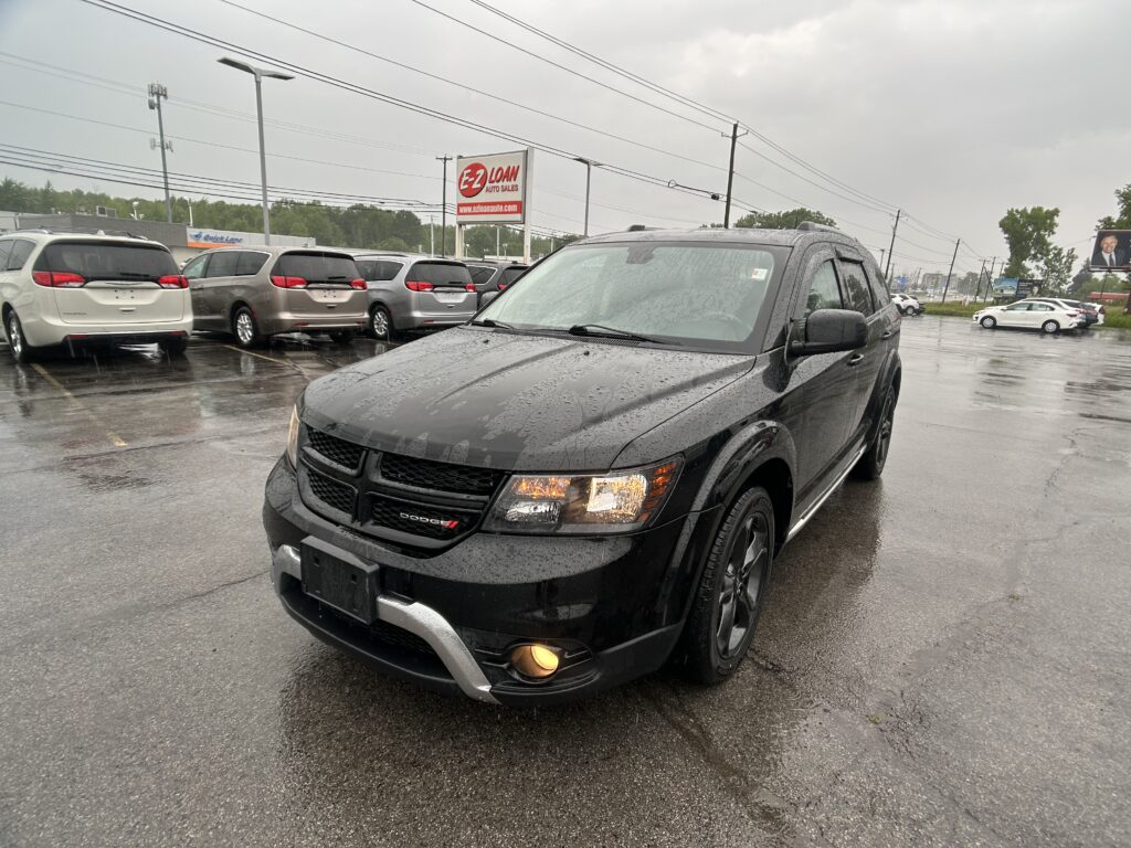 Black Dodge SUV in the foreground on a rainy dealership lot, with minivans parked in the background and an E-Z Loan Auto Sales sign visible in the distance.