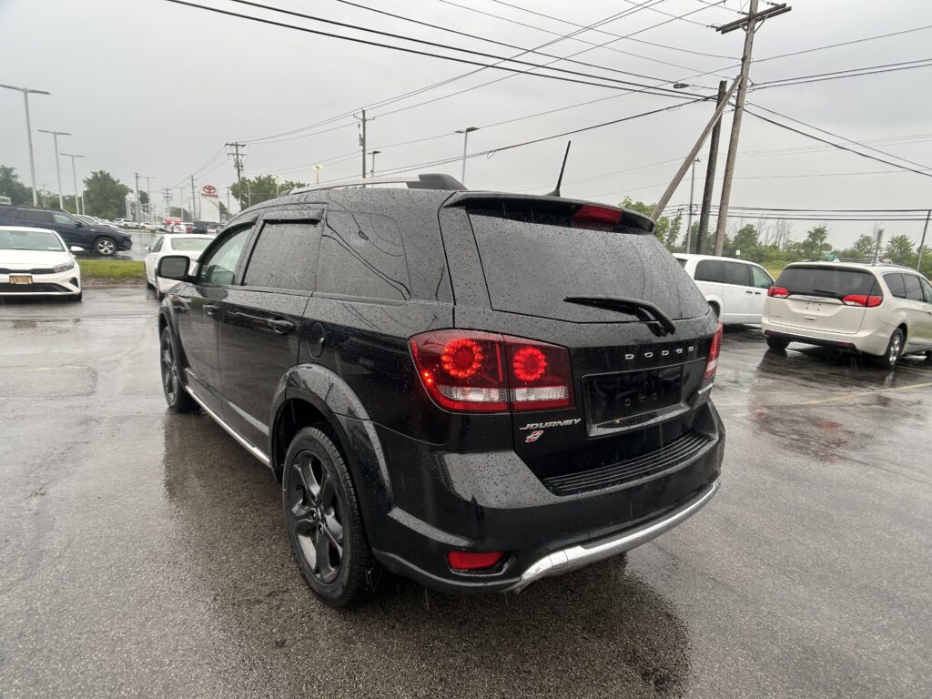 Rear three-quarter view of a black Dodge Journey SUV in a rainy parking lot, raindrops on the windows and taillights glowing red.