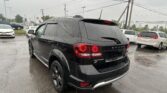Rear three-quarter view of a black Dodge Journey SUV in a rainy parking lot, raindrops on the windows and taillights glowing red.