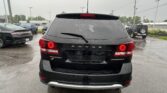 Rear view of a black Dodge Journey SUV in a wet parking lot after rain, with other vehicles and power lines in the background.