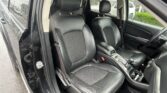 Black leather front seats in a car with headrests and center console, rain on the windows outside.