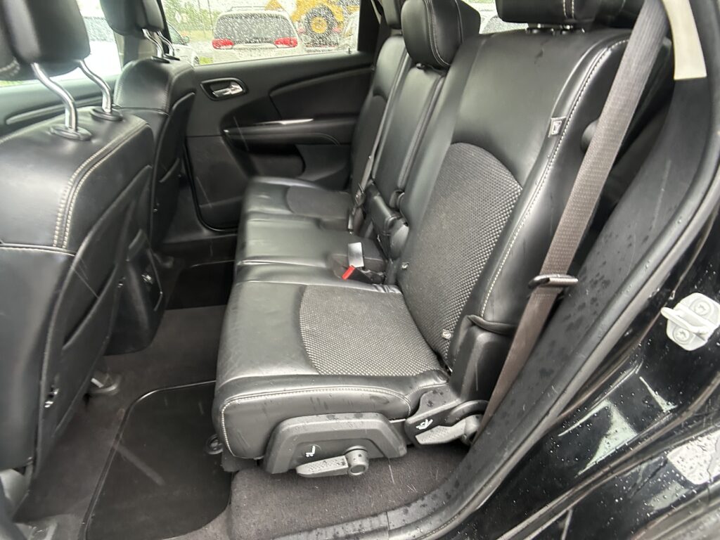 Interior of a black leather SUV rear seat row with three seats, headrests, and visible seat belts behind the front seats.