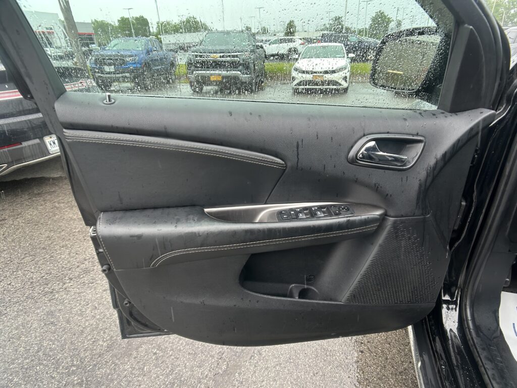 Car door interior with water droplets on the window; view of parked cars in a lot outside outside.