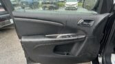 Car door interior with water droplets on the window; view of parked cars in a lot outside outside.