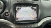 Rearview camera display: wet parking lot with guiding lines and a warning to check surroundings.