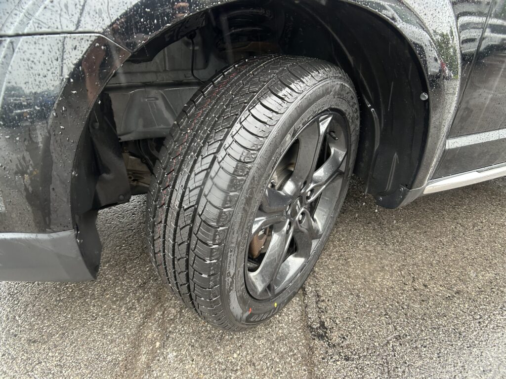 Close-up of a wet car wheel and tire in a wheel well after rain, showing tread pattern and wheel rim.