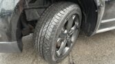 Close-up of a wet car wheel and tire in a wheel well after rain, showing tread pattern and wheel rim.