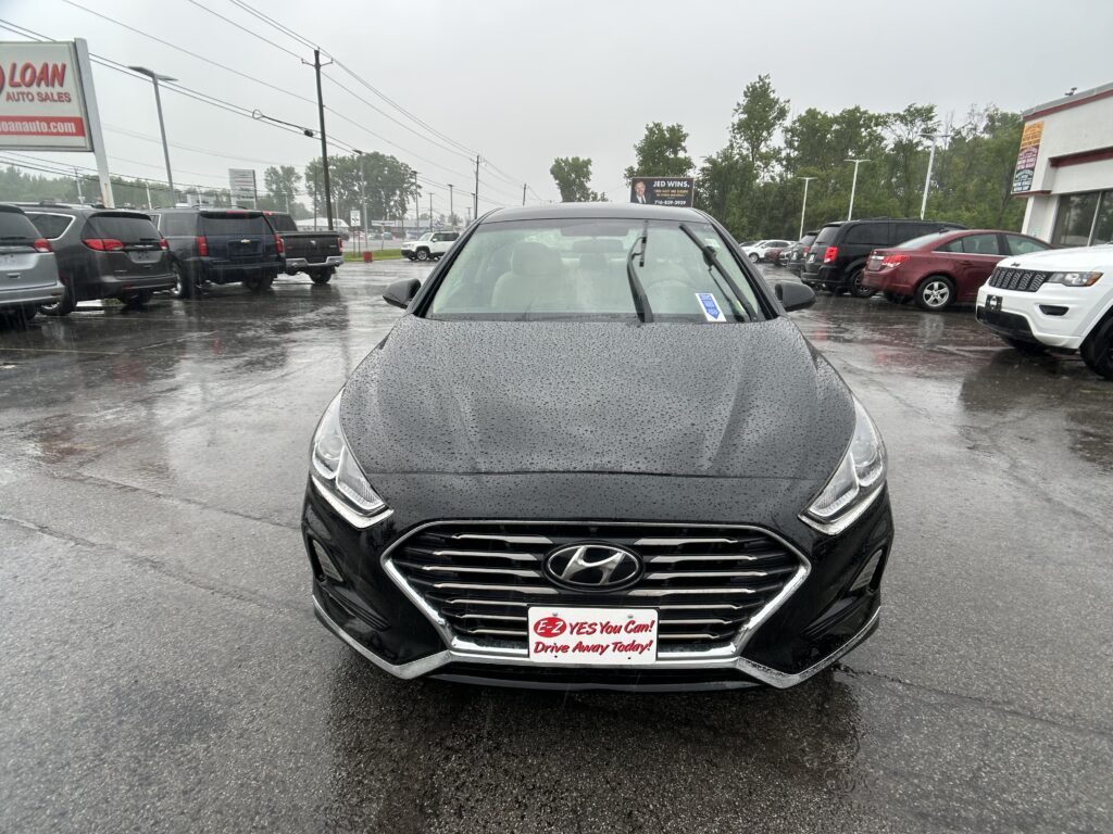 Front view of a black Hyundai in a rainy dealership lot, promotional plate reading 'E-Z YES You Can! Drive Away Today!'.