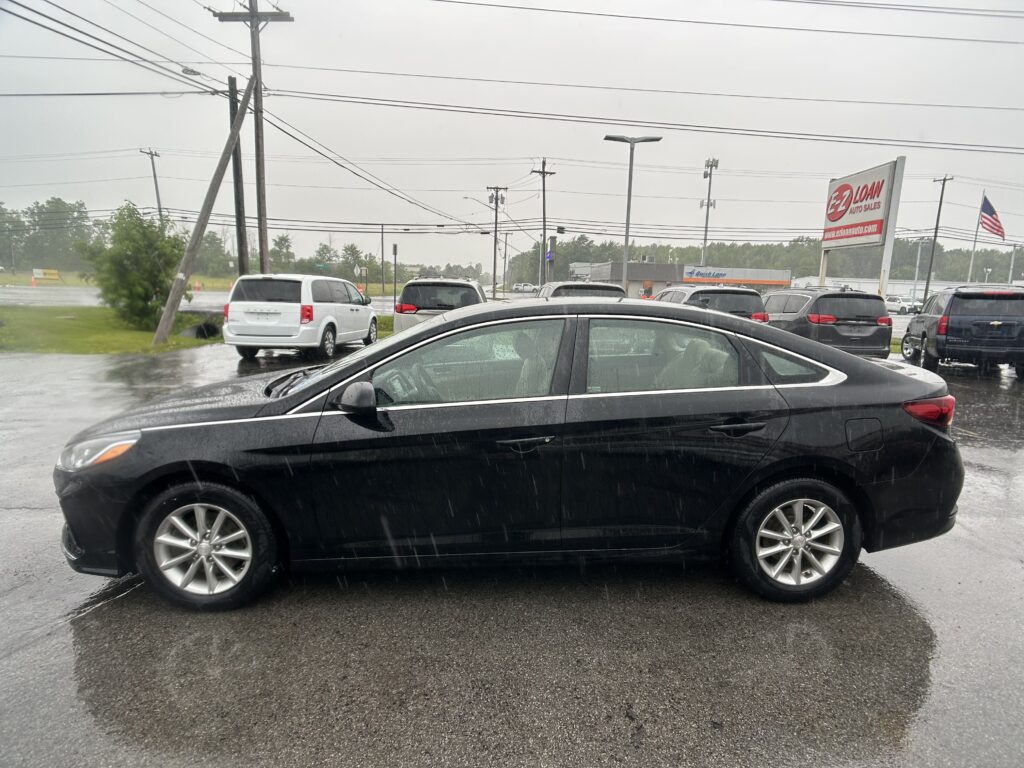 Rainy day at a car lot with multiple parked cars and a tall EZ LOAN Auto Sales sign in the background.