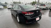Rear view of a black Hyundai Sonata in a wet dealership lot with white and silver cars in the background during rain.