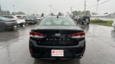 Rear view of a black Hyundai Sonata in a wet parking lot during rain, with other cars around and a dealership plate reading 'EZ Yes You Can! Drive Away Today!'