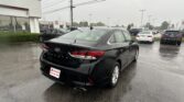 Black Hyundai Sonata in foreground at a rainy dealership lot with other cars and a Toyota dealership building in the background.