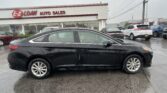 Black sedan in foreground at a car dealership lot with a white building reading 'E-Z LOAN AUTO SALES' in the background on a rainy day