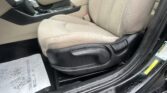 Front passenger seat and center console of a beige car interior, with the gear shifter and door sill visible, and moisture on the floor mats and door edge.