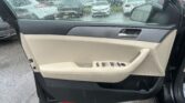 Interior of a car door with beige and gray panels, window partly down in heavy rain outside the car
