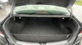 Open black car trunk with empty cargo area; rain on rear window and outside cars visible in a parking lot.