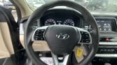 Driver's view of a car interior with steering wheel, dashboard gauges, and a rainy windshield outside the car window.