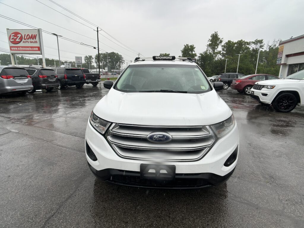 Front view of a white Ford SUV in a rainy car dealership lot with an E-Z Loan Auto Sales sign in the background.