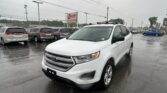 White Ford SUV in the foreground at a rainy used-car lot, with several minivans parked behind and power lines overhead near an EZ LOAN Auto Sales sign.
