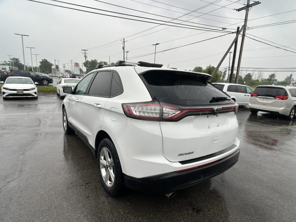 White Ford Edge SUV parked in a wet dealership lot with power lines overhead.