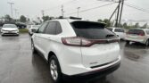 White Ford Edge SUV parked in a wet dealership lot with power lines overhead.