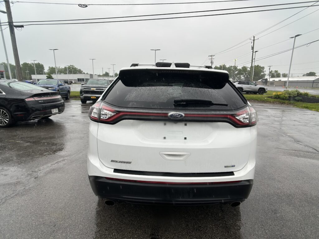 Rear view of a white Ford Edge SUV in a wet parking lot on a rainy day.