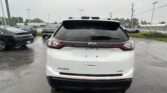Rear view of a white Ford Edge SUV in a wet parking lot on a rainy day.