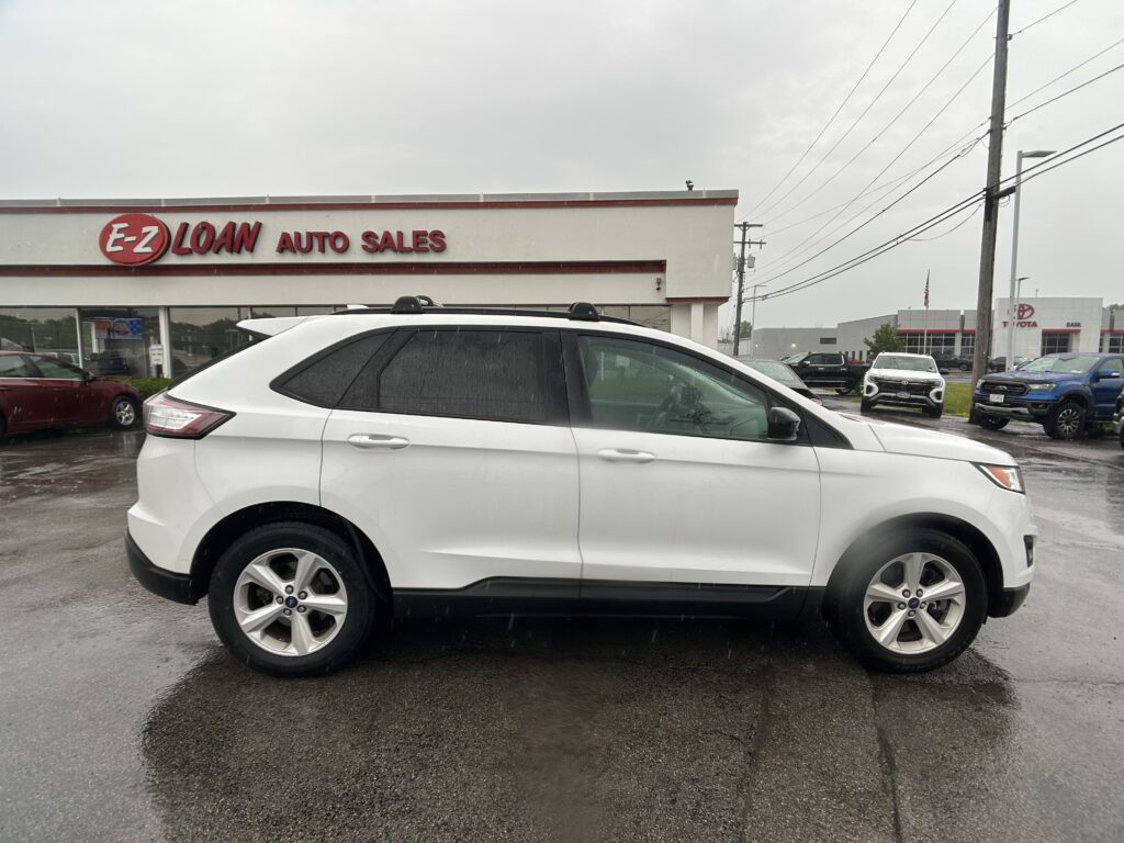 White SUV parked in front of E-Z Loan Auto Sales on a cloudy, rainy day with other vehicles and the dealership sign in view.
